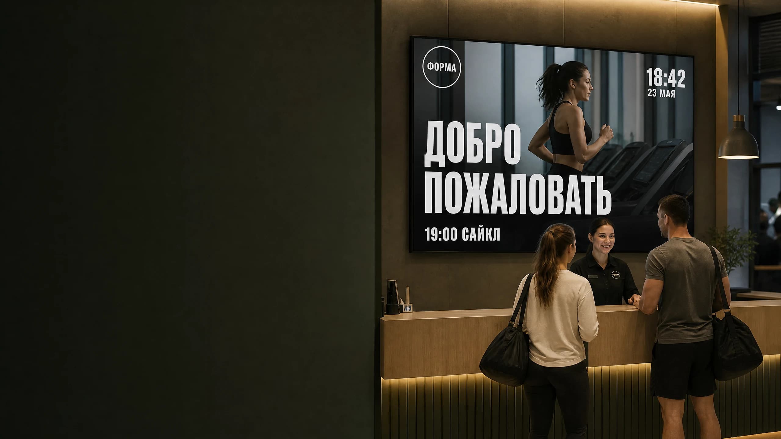 Экран на ресепшн фитнес-клуба: приветствие, ближайшее групповое занятие и часы, администратор встречает гостей клуба