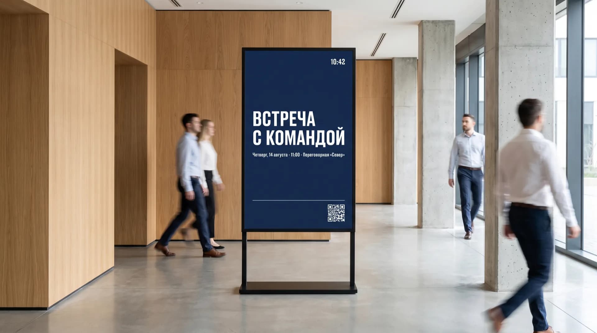 Вертикальная панель в холле бизнес-центра показывает объявление «Встреча с командой» с датой, временем, переговорной, часами и QR-кодом; мимо идут сотрудники